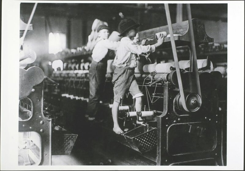 Two young boys standing on electric looms in order to reach the top shelf while at work in a cotton mill in Georgia.