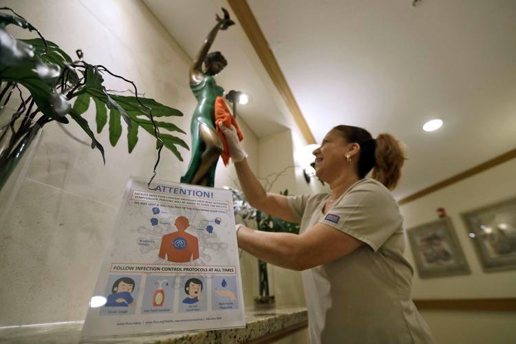 Environmental Services member Maggie Masstrapa cleans behind an infection control warning poster at the Palm Garden of Tampa Health and Rehabilitation Center on Thursday, March 5, 2020, in Tampa, Fla. Chris O'Meara / AP