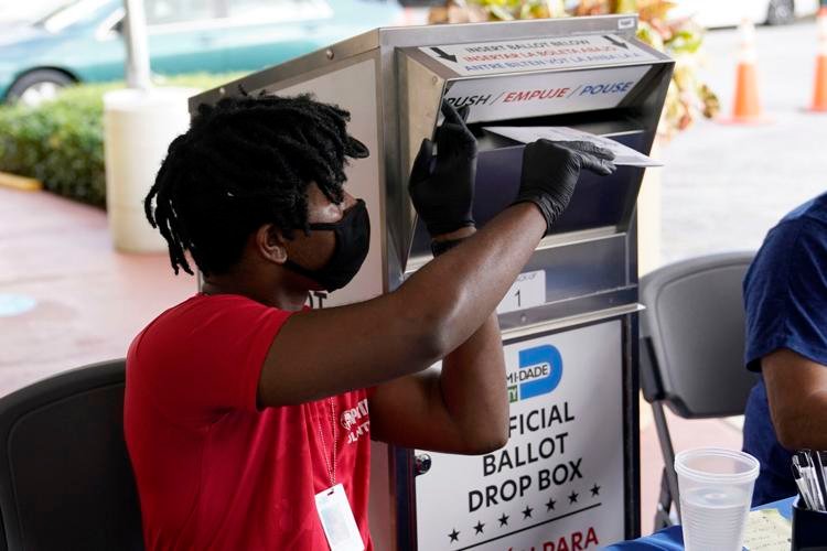 Election worker Najeh Fisher places a vote-by-mail ballot for the Nov. 3 general election into an official ballot drop box at the Miami-Dade County Elections Department on Wednesday, Oct. 14, 2020, in Doral, Fla. Lynne Sladky / AP