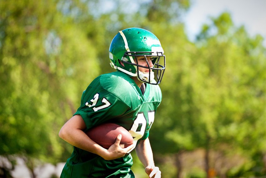 A high school or university American football player playing in an outdoor football field. He is carrying a football running.