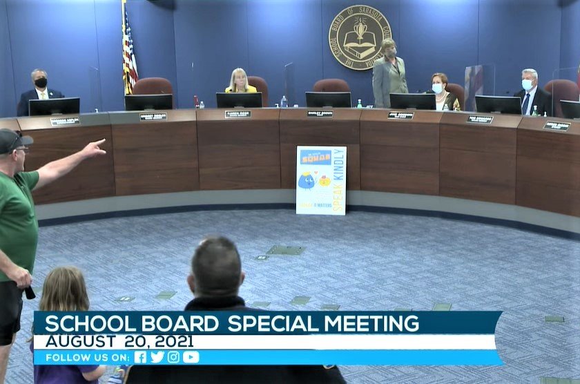 John Wilson, who opposes mask mandates, shouts at Sarasota County School Board chair and former state Rep. Shirley Brown (standing), who called a recess to clear the room of hecklers. Screenshot: Sarasota County School Education Channel