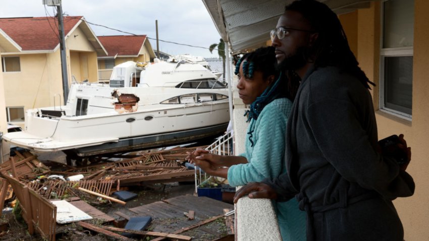 Frankie Romulus (L) and Kendrick Romulus stand outside of their apartment next to a boat that floated into their apartment complex when Hurricane Ian passed through the area on September 29th in Ft. Myers.