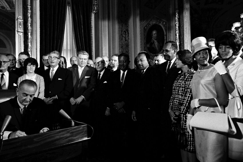 President Lyndon B. Johnson signs the Voting Rights Act of 1965 while Martin Luther King and others look on.
