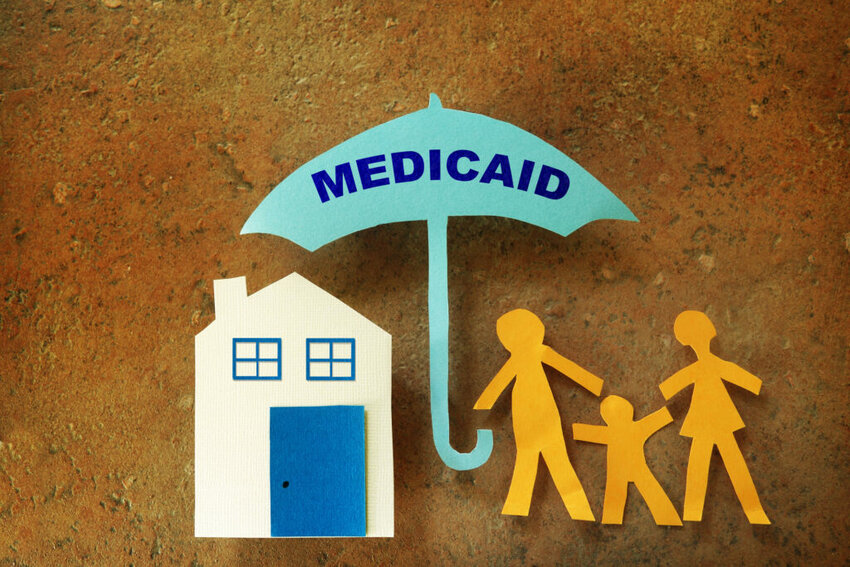 Paper cutout family with house under a Medicaid umbrella
