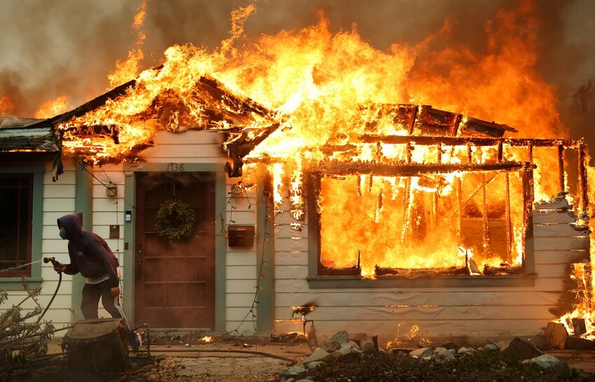 A person uses a garden hose in an effort to save a neighboring home from catching fire during the Eaton Fire on Jan. 8, 2025 in Altadena, California.
