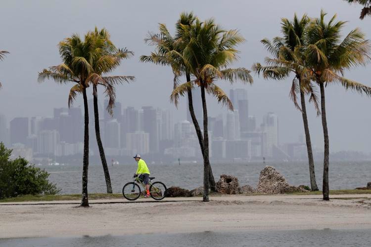 The Miami skyline is shrouded in clouds Friday, May 15, 2020, as a cyclist rides along Biscayne Bay at Matheson Hammock Park in Miami. National Oceanic and Atmospheric Administration's Climate Prediction Center, said Thursday six to 10 storms could develop into hurricanes this season. Lynne Sladky / AP