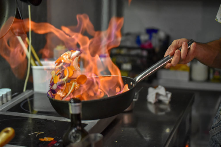 Chef tossing vegetables flambe in a pan over the burner