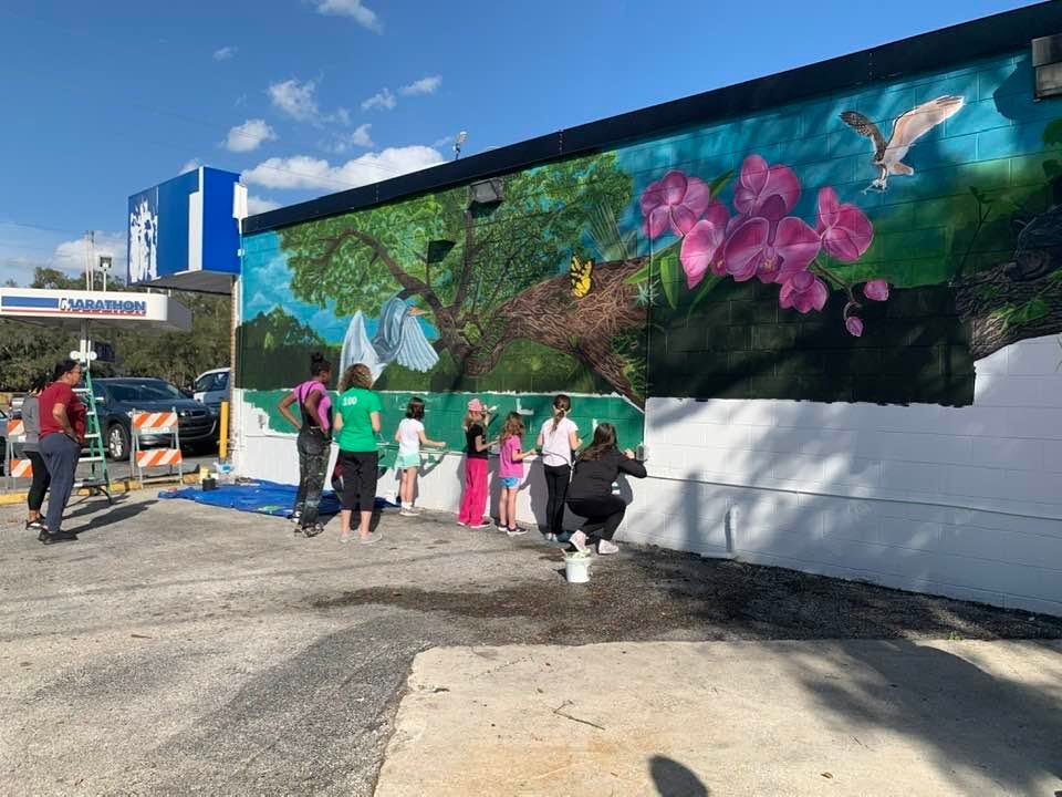Artist Delia Miller stands with students from Clay Springs Elementary School at mural on Thompson Road in Apopka
