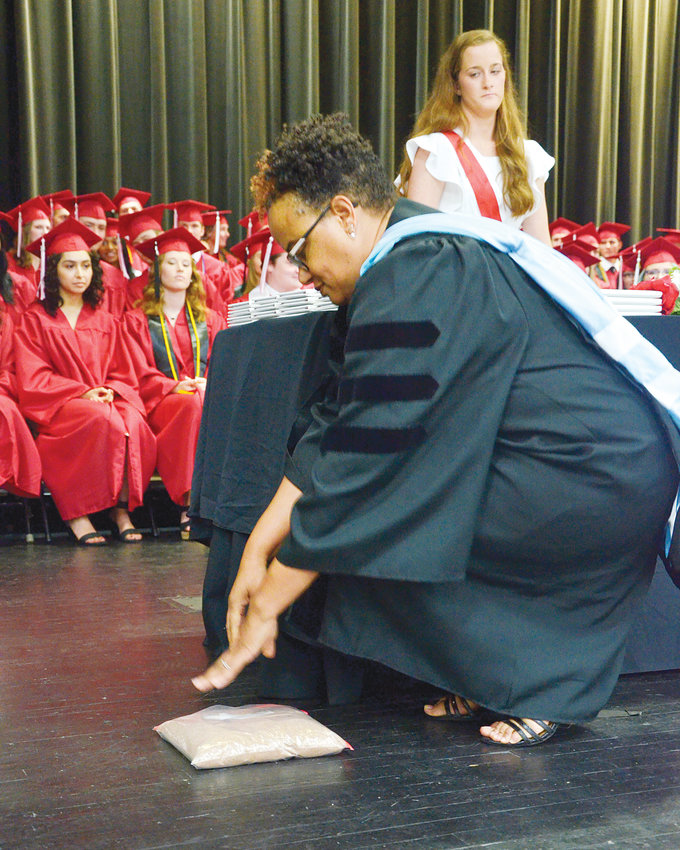 As one of the marshals and the students look on, Dr. Karla Eanes, principal of Chatham Central High School, places a bag of Chatham County soil on the stage in the civic center in Sanford Friday night. The bag was brought so that each student would graduate on Chatham County soil, Dr. Eanes said.