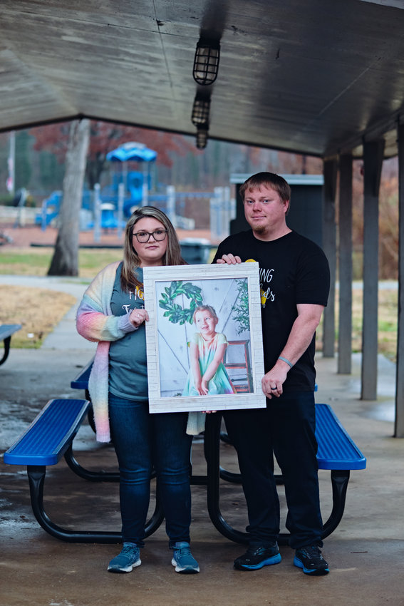 Meghan and Dusty Scoggins pose with a framed photo of their 5-year-old daughter Kenzie, who died from an aggressive brain tumor called diffuse intrinsic pontine glioma in September.