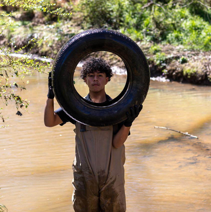 Marlon Interiano, volunteer from CIS, picks a tire out of the muddy Loves Creek Saturday.