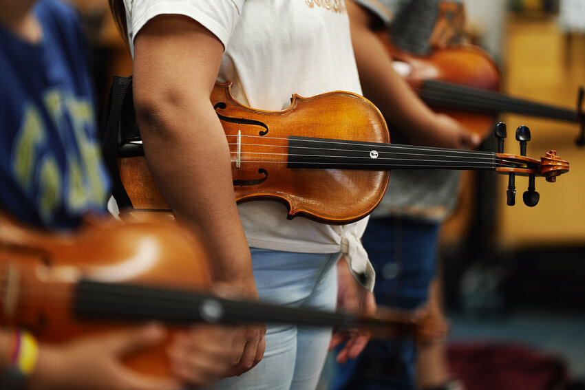 Students carefully cradle their violins under their arms in the 'rest position.'