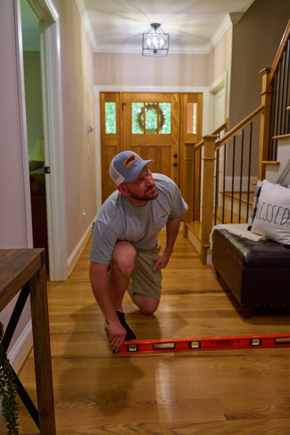 Jake Muehlbach shows how his floors are bowed using a leveler. The flooring is one of more than 30 code violations in the home.