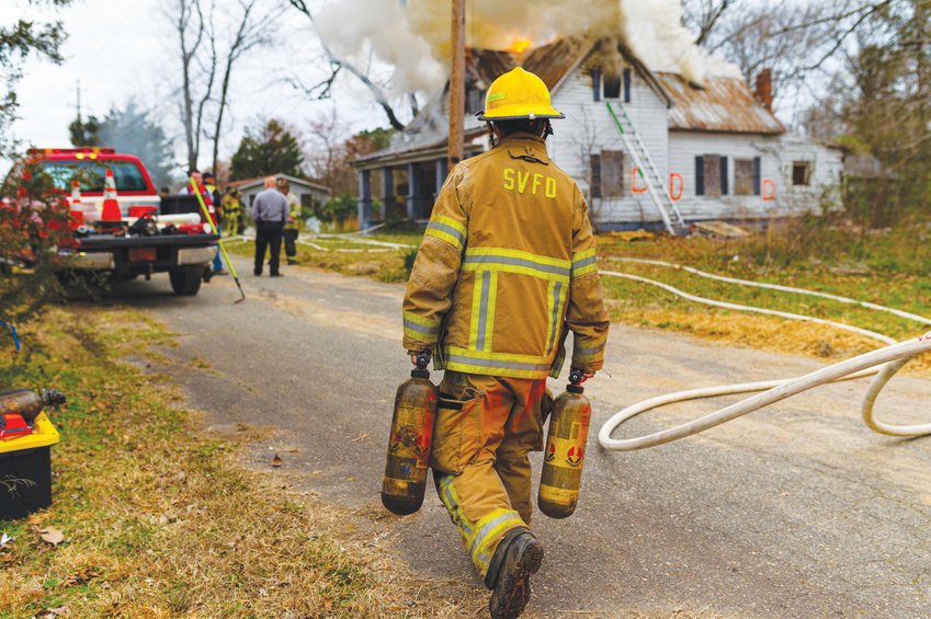 A Siler City Fire Department member carries oxygen tanks to the lineup of roughly 40 firefighters from several area departments. The firefighters performed a controlled burn on a house on E. 11th Street earlier this year.