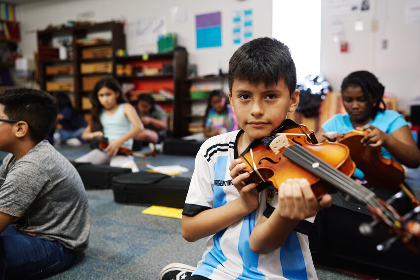 Miguel, a student in the after school strings program at Siler City Elementary School, sits eagerly with the violin under his chin. He practices holding the violin in the correct position.