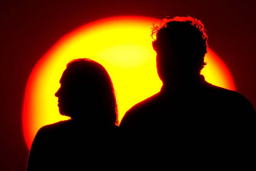 A couple watches the sunset from a park, July 10, 2021, in Kansas City, Mo. (AP Photo/Charlie Riedel, File)