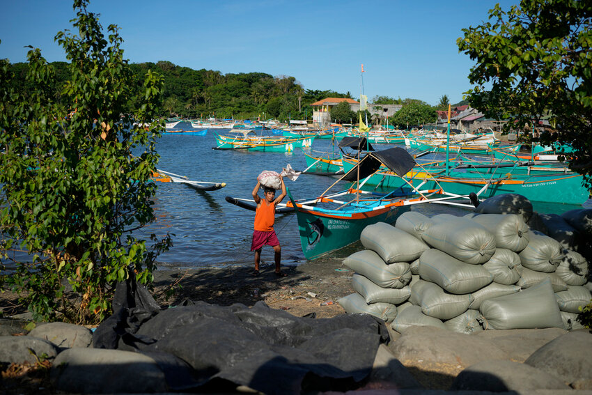 A resident brings down a sack from his boat at the coastal town of Santa Ana, Cagayan province, northern Philippines on Tuesday, May 7, 2024. (AP Photo/Aaron Favila)