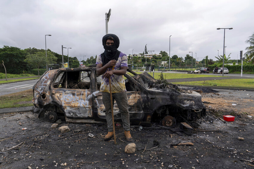A man stands in front a burned car after unrest in Noumea, New Caledonia, Wednesday, May 15, 2024. (AP Photo/Nicolas Job)