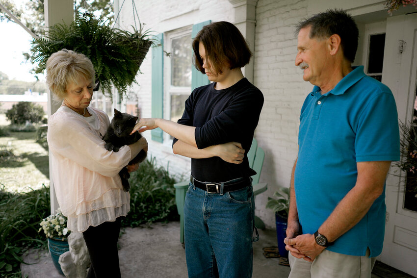 Jesse Fernandez, center, pets the family cat as he visits his former foster parents Jason and Joyce White Friday, May 17, 2024, in Independence, Mo. Fernandez was paid thousands of dollars of Social Security survivor's benefits because of the death of his mother, but by the time he turned 18, the money had all been used by the state of Missouri and Fernandez's relatives to pay for his foster care. (AP Photo/Charlie Riedel)