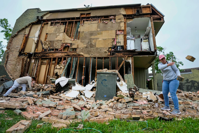 David Figueroa, left, and Delmy Suazo toss bricks to a pile as they work to clean up debris after a wall came down at an apartment complex in the aftermath of a severe storm on Friday, May 17, 2024 in Houston. (Brett Coomer/Houston Chronicle via AP)