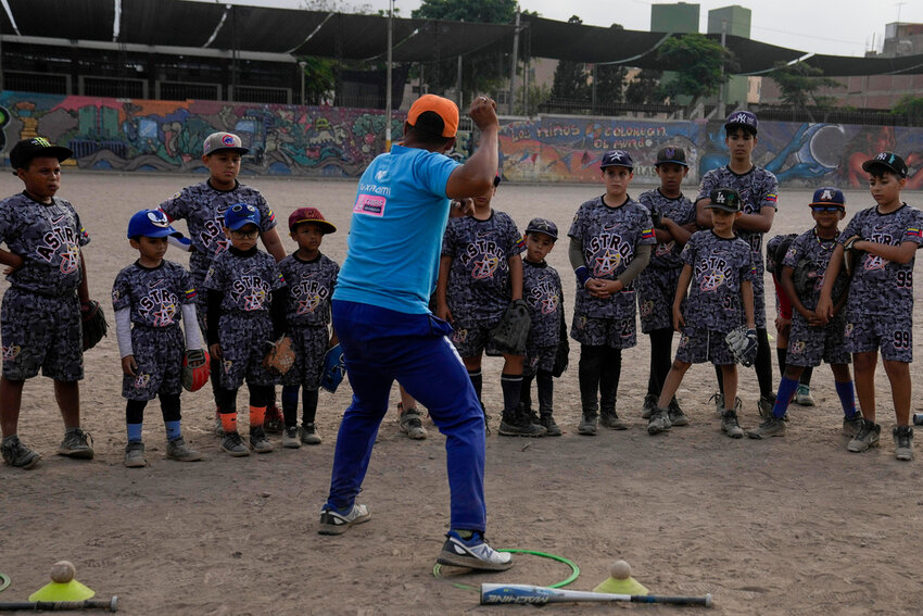 Baseball coach Franklin Lopez shows young Venezuelan migrants how to throw a ball during a baseball practice session in a public park in the Comas area, on the outskirts of Lima, Peru, Thursday, May 2, 2024. Immigrants, mainly Venezuelans, have opened five baseball academies in Peru's capital. (AP Photo/Martin Mejia)