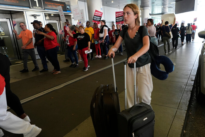 A traveler walks through the departure area as airline catering workers who are employed by Gate Gourmet picket with their supporters, Wednesday, July 3, 2024, at Miami International Airport in Miami. (AP Photo/Lynne Sladky)