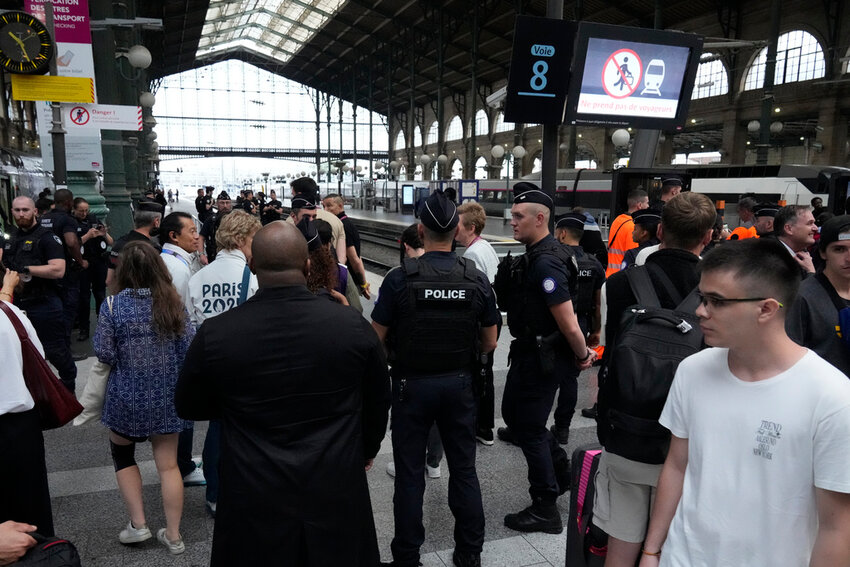 Travelers wait as police officers patrol inside the Gare du Nord train station Friday, July 26, 2024, in Paris. (AP Photo/Mark Baker)
