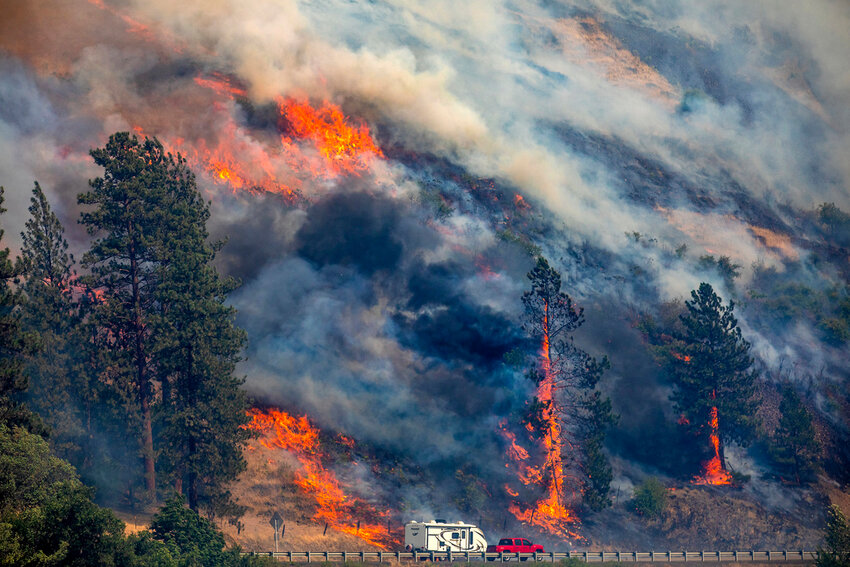 A vehicle drives past the spreading River Fire Thursday, July 25, 2024, near Myrtle, Idaho, before U.S. Highway 12 was closed. (August Frank/Lewiston Tribune via AP)