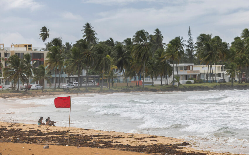 Tourists sit on La Pared beach as Tropical Storm Ernesto passes by Luquillo, Puerto Rico, Tuesday, Aug. 13, 2024. (AP Photo/Alejandro Granadillo)