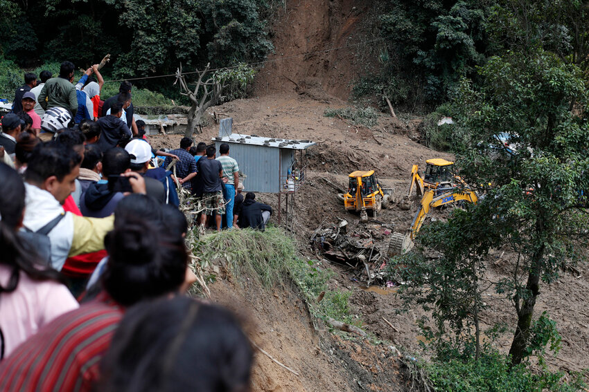 People watch earthmovers removing automobile debris and the dead bodies of victims  trapped under a landslide caused by heavy rains in Kathmandu, Nepal, Sunday, Sept. 29, 2024. (AP Photo/Sujan Gurung)