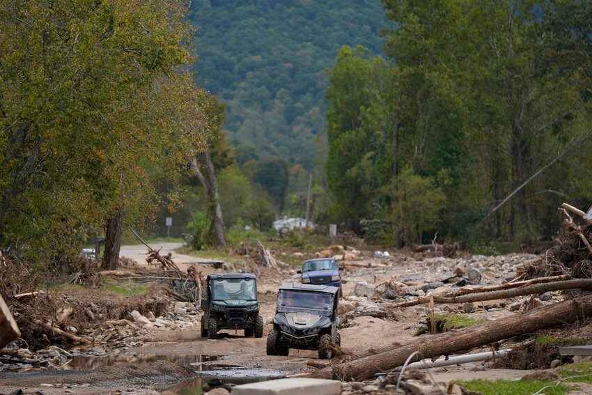 Vehicles roll along on a washed up road in the aftermath of Hurricane Helene, Thursday, Oct. 3, 2024, in Pensacola, N.C. (AP Photo/Mike Stewart)