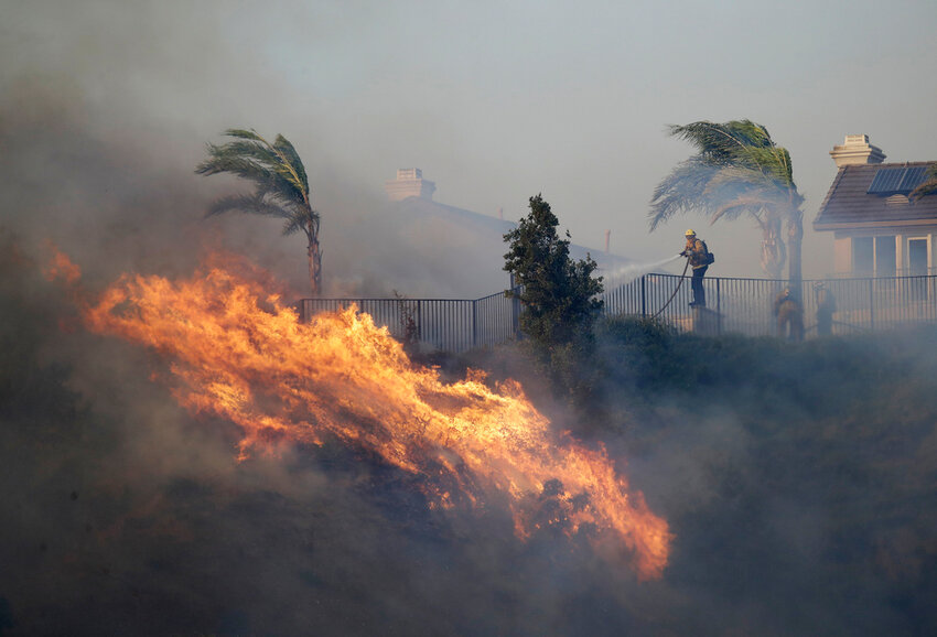 FILE - A firefighter sprays water in front of an advancing wildfire Friday, Oct. 11, 2019, in Porter Ranch, Calif. (AP Photo/Marcio Jose Sanchez, File)