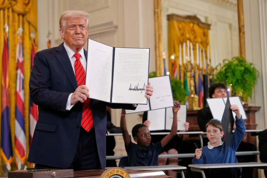 President Donald Trump holds up a signed executive order as young people hold up copies of the executive order they signed at an education event in the East Room of the White House in Washington, Thursday, March 20, 2025. (AP Photo/Ben Curtis)