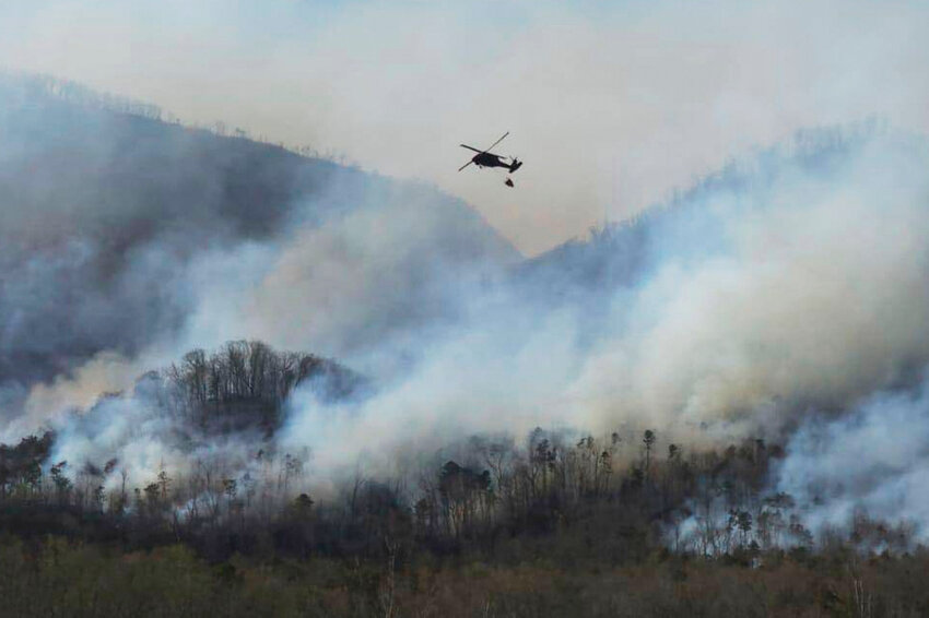 A UH-60 Black Hawk helicopter from the 1-111th General Support Aviation Battalion, 59th Aviation Troop Command, McEntire Joint National Guard Base in Eastover executes a fire suppression mission in support of the South Carolina Forestry Commission at Persimmon Ridge Fire near Greenville, S.C., on Sunday, March 23, 2025. (Sgt. 1st Class Roberto Di Giovine/U.S. Army National Guard via AP)