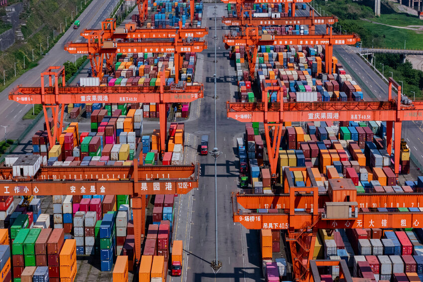 Trucks move past piles of containers stacked at a container terminal port on the Yangtze River in southwest China's Chongqing Municipality on Sunday, April 20, 2025. (Chinatopix Via AP)