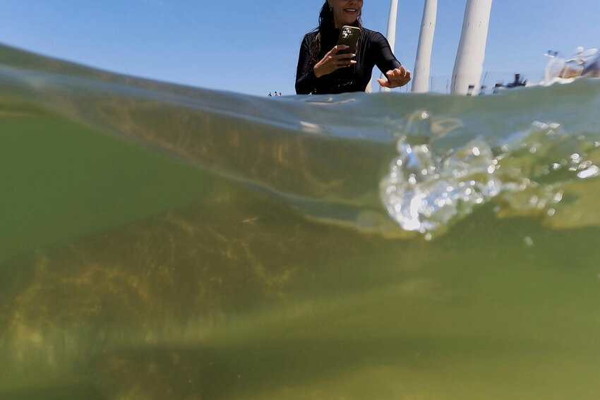 A woman reaches out to a shark swimming in the Mediterranean Sea in Hadera, Israel, Saturday, April 19, 2025. (AP Photo/Ariel Schalit)