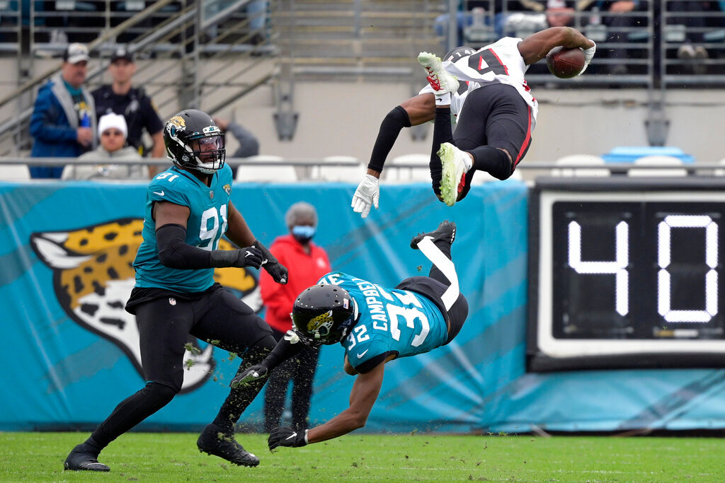 Atlanta Falcons wide receiver Russell Gage, top right, leaps over Jacksonville Jaguars cornerback Tyson Campbell (32) and defensive end Dawuane Smoot, left, after a reception during the first half of an NFL football game, Sunday, Nov. 28, 2021, in Jacksonville, Fla. (AP Photo/Phelan M. Ebenhack)