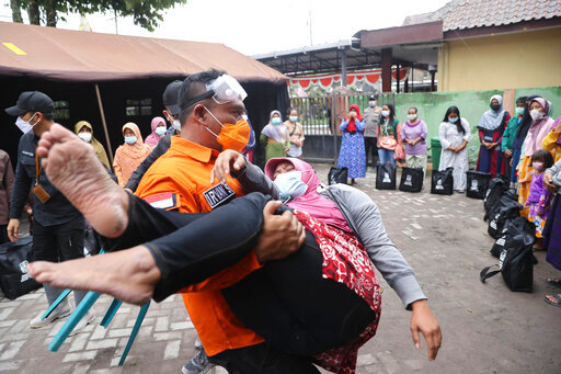 A rescuer holds a woman who fell down in a faint, after seeing her house destroyed by the eruption of Mount Semeru in Lumajang district, East Java province, Indonesia, Sunday, Dec. 5, 2021. The death toll from the eruption of the highest volcano on Indonesia's most populous island of Java has risen by a score of still missing, officials said Sunday as rain continued to lash the area and hamper the search. (AP Photo/Trisnadi)