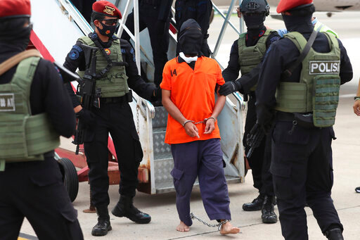 FILE - Police officers escort suspected Islamic militant Upik Lawanga, center, upon arrival following his arrest, at Soekarno-Hatta International Airport in Tangerang, Indonesia, on Wednesday, Dec. 16, 2020. An Indonesian court sentenced Lawanga who eluded capture for 16 years to life in prison on Wednesday after finding him guilty of making bombs used in a 2005 market attack that killed 22 people. (AP Photo/Achmad Ibrahim, File)