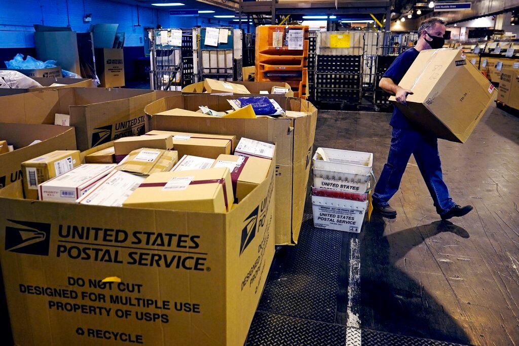 FILE- A worker carries a large parcel at the United States Postal Service sorting and processing facility, Thursday, Nov. 18, 2021, in Boston. The U.S Postal Service pulled out all the stops to avoid a repeat of the 2020 holiday shipping disaster, and it worked. The Postal Service and several other private shippers reported that holiday season deliveries went smoothly, for the most part. (AP Photo/Charles Krupa, File)