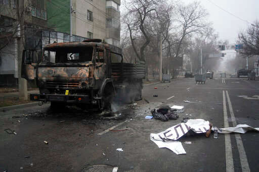 A body of victim covered by a banner, right, lays near to a military truck, which was burned after clashes, in Almaty, Kazakhstan, Thursday, Jan. 6, 2022. Kazakhstan's president authorized security forces on Friday to shoot to kill those participating in unrest, opening the door for a dramatic escalation in a crackdown on anti-government protests that have turned violent. The Central Asian nation this week experienced its worst street protests since gaining independence from the Soviet Union three decades ago, and dozens have been killed in the tumult. (AP Photo/Vladimir Tretyakov/NUR.KZ via AP)