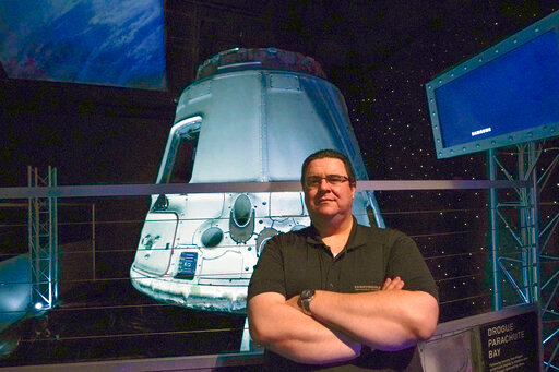Kyle Hippchen, a Florida-based airline captain, poses for a photo in front of a SpaceX Dragon capsule at the Kennedy Space Center Visitor Complex in Cape Canaveral, Fla., Friday, Jan. 21, 2022. Hippchen, the real winner of a first-of-its-kind sweepstakes, gave his seat on a SpaceX flight to his college roommate. Though his secret is finally out, that doesn’t make it any easier knowing he missed his chance to orbit Earth because he exceeded the weight limit. (AP Photo/John Raoux)