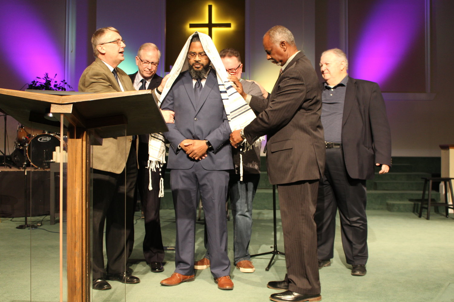 Retiring Liberty Pastor Randy Wood (left) passes the prayer shawl or mantel on to new pastor James Oney (center) with the help of Deacon Chairman George Smith.
