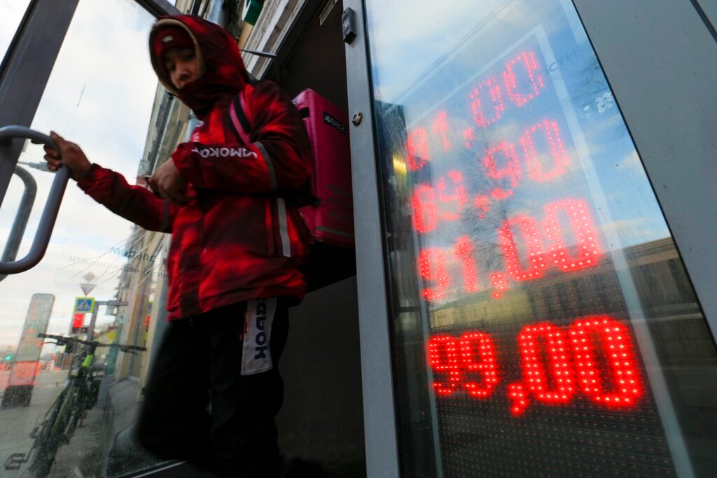 A food delivery man leaves an exchange office with screen showing the currency exchange rates of U.S. Dollar and Euro to Russian Rubles in Moscow, Russia, Thursday, Feb. 24, 2022. The ruble plunged to a record low of less than 1 U.S. cent in value Monday after Russia was cut off from the global bank payments system in retaliation for Moscow’s invasion of Ukraine. (AP Photo/Alexander Zemlianichenko Jr.,File)