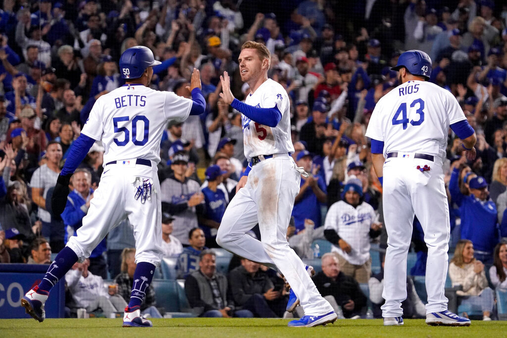 Los Angeles Dodgers' Freddie Freeman, center, is congratulated by Mookie Betts, left, and Edwin Rios after they scored on a double by Trea Turner during the fourth inning of a baseball game against the Atlanta Braves Monday, April 18, 2022, in Los Angeles. (AP Photo/Mark J. Terrill)