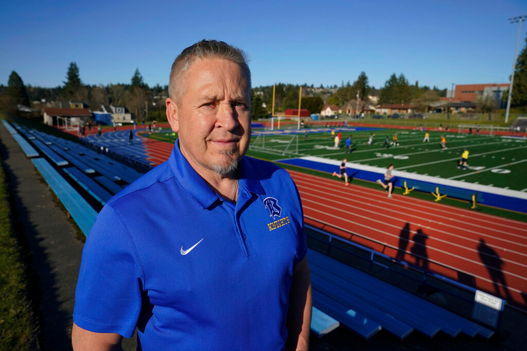 Joe Kennedy, a former assistant football coach at Bremerton High School in Bremerton, Wash., poses for a photo March 9, 2022, at the school's football field. After losing his coaching job for refusing to stop kneeling in prayer with players and spectators on the field immediately after football games, Kennedy will take his arguments before the U.S. Supreme Court on Monday, April 25, 2022, saying the Bremerton School District violated his First Amendment rights by refusing to let him continue praying at midfield after games. (AP Photo/Ted S. Warren)