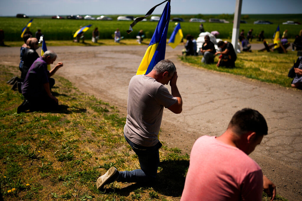 Mourners kneel as they wait for the coffin of Volodymyr Losev to pass during his funeral in Zorya Truda, Odesa region, Ukraine, Monday, May 16, 2022. Losev, a Ukrainian volunteer soldier, was killed May 7 when the military vehicle he was driving ran over a mine in eastern Ukraine. (AP Photo/Francisco Seco)