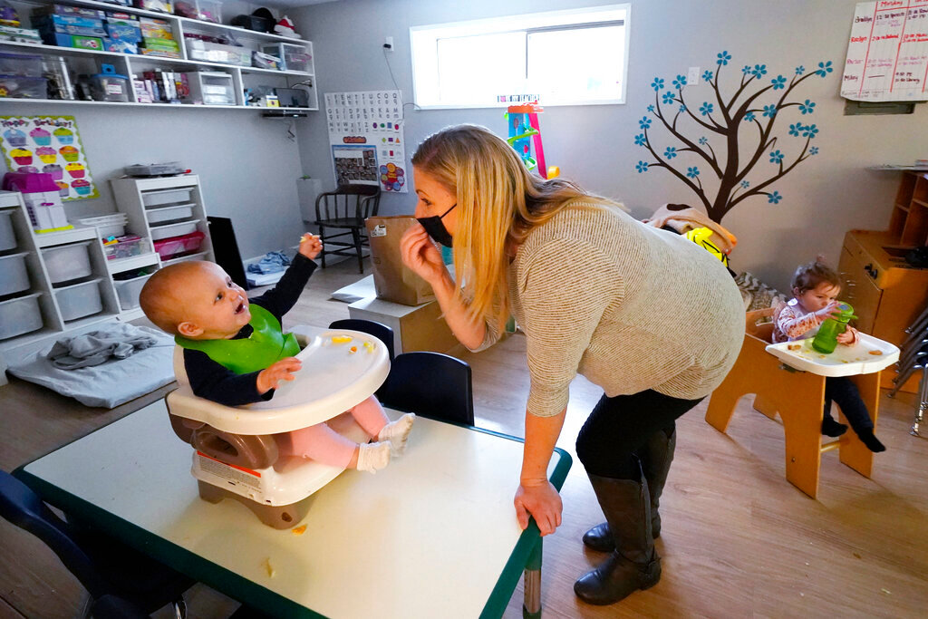 Amy McCoy signs to a baby about food as a toddler finishes lunch behind at her Forever Young Daycare facility, Monday, Oct. 25, 2021, in Mountlake Terrace, Wash. (AP Photo/Elaine Thompson, File)