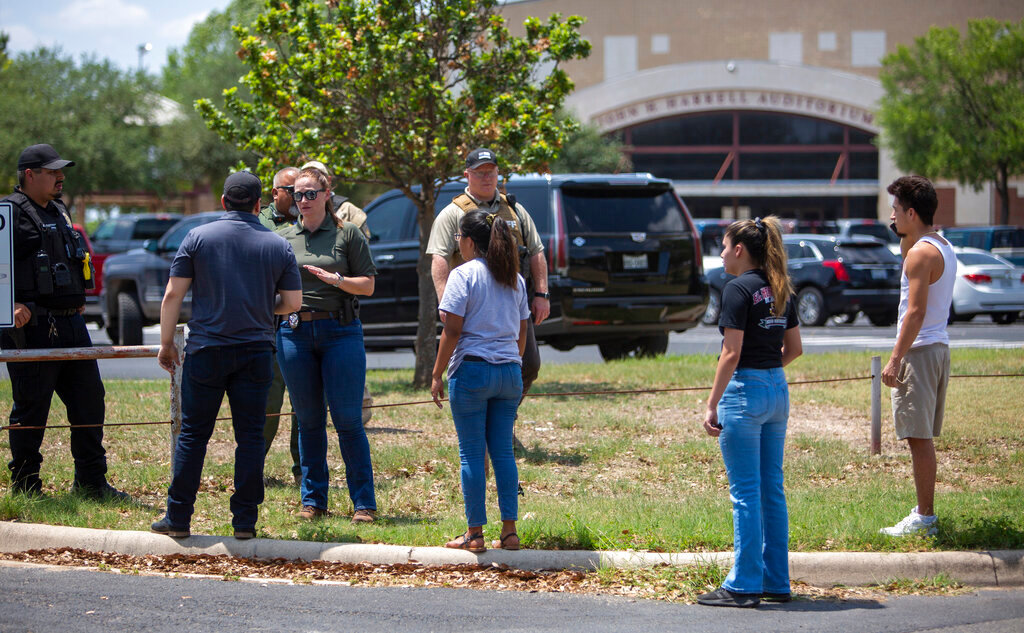 A police officer speaks with people outside Uvalde High School after shooting a was reported earlier in the day at Robb Elementary School, Tuesday, May 24, 2022, in Uvalde, Texas. (William Luther/The San Antonio Express-News via AP)