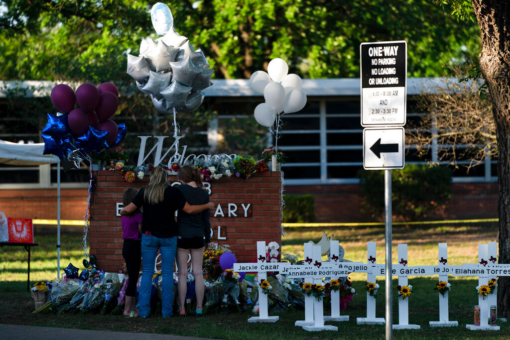 A family pays their respects next to crosses bearing the names of Tuesday's shooting victims at Robb Elementary School in Uvalde, Texas, Thursday, May 26, 2022. (AP Photo/Jae C. Hong)